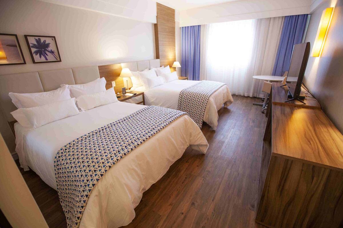 A hotel room with two beds, a desk, and a chair.
