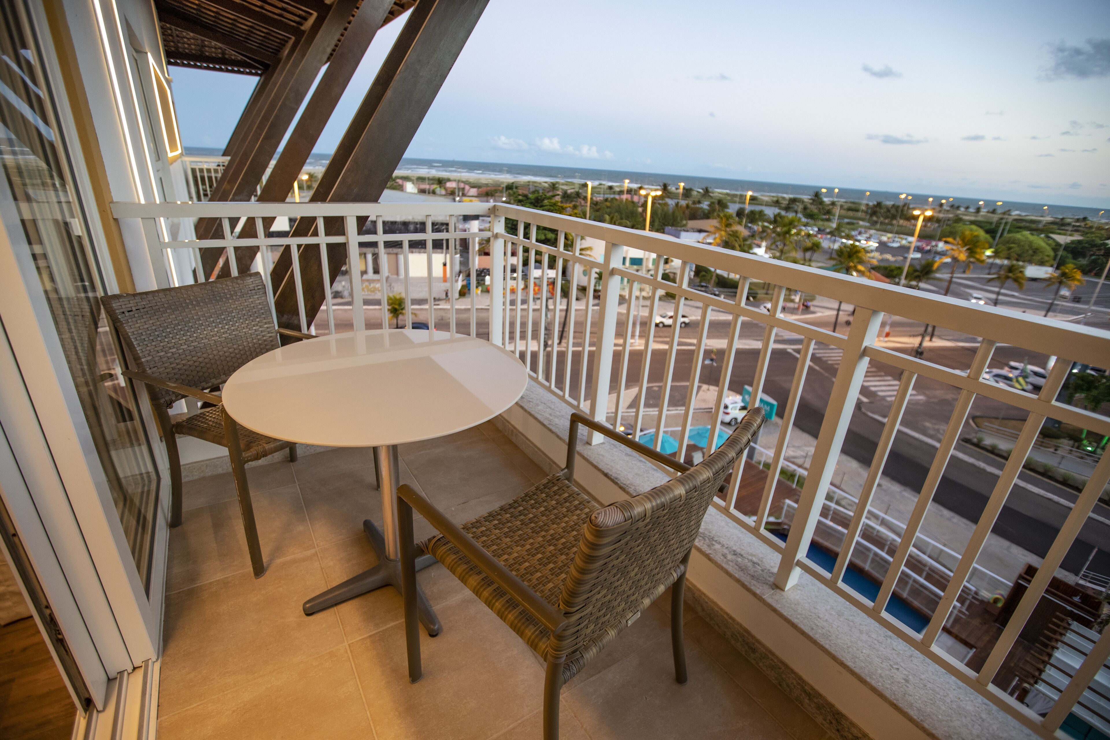A balcony with a table and chairs, overlooking a pool and a view of the city.