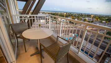 A balcony with a table and chairs, overlooking a pool and a view of the city.