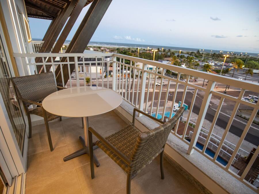 A balcony with a table and chairs, overlooking a pool and a view of the city.