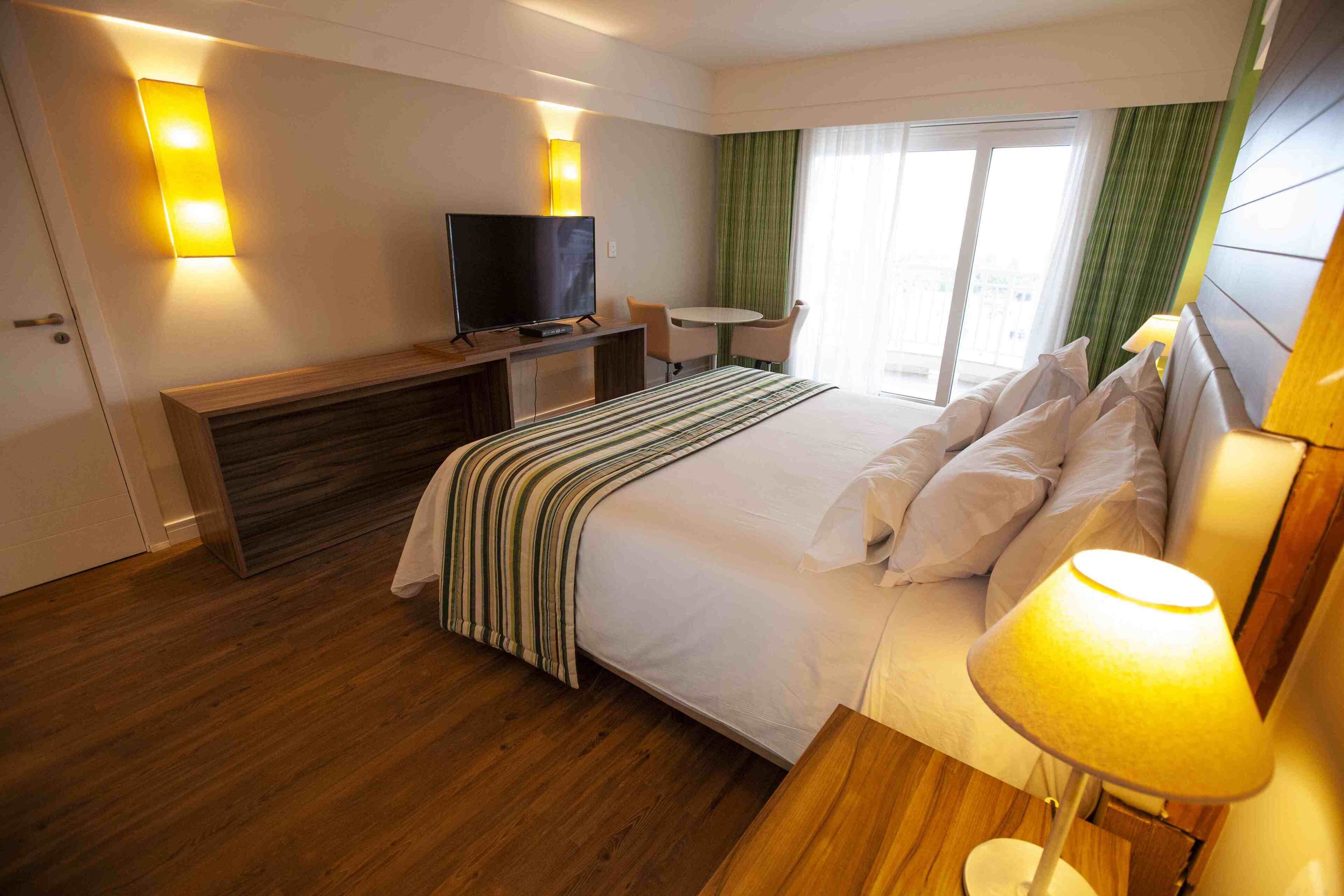 Une chambre d’hôtel avec un lit, une télévision, un bureau et une fenêtre avec des rideaux.