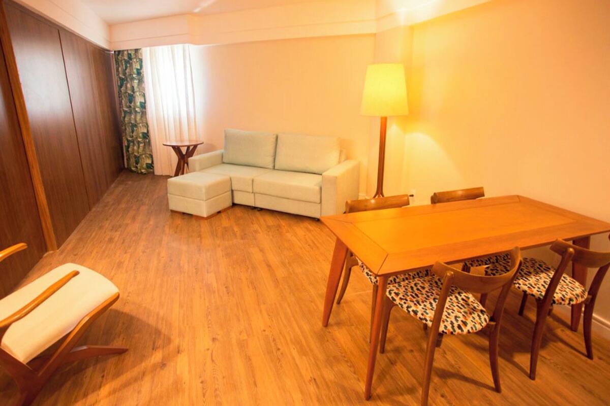 A room with a wooden dining table, four chairs, a sofa, and a lamp.