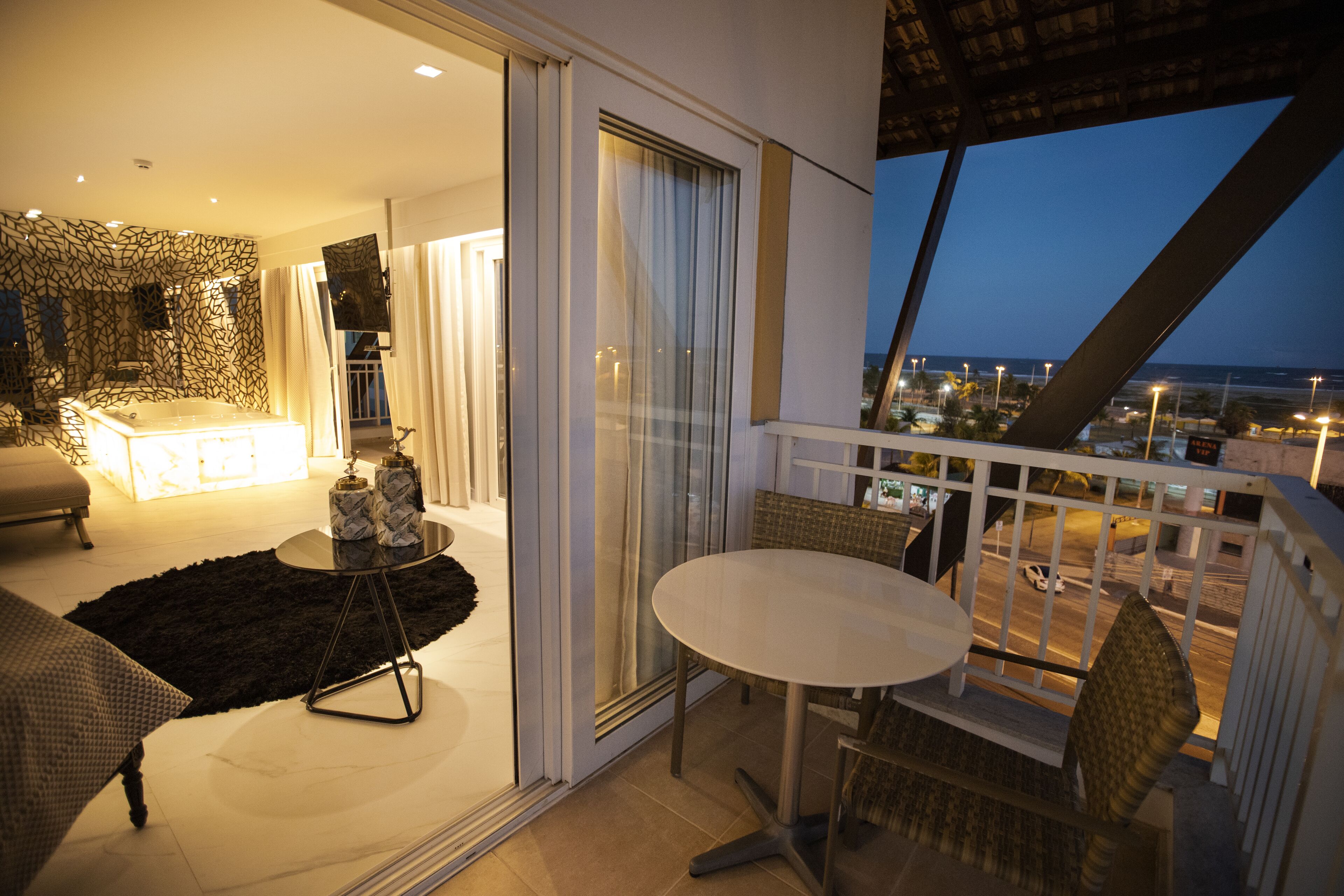 Un balcón con mesa y sillas, vista a la ciudad, e interior moderno con sofá y televisor.