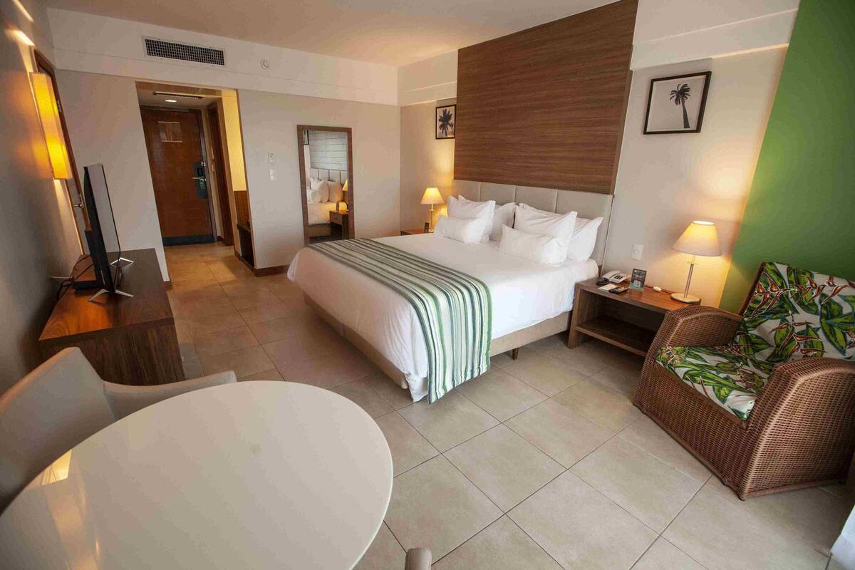 A hotel room with a bed, bedside table, lamp, chair, and a round table.