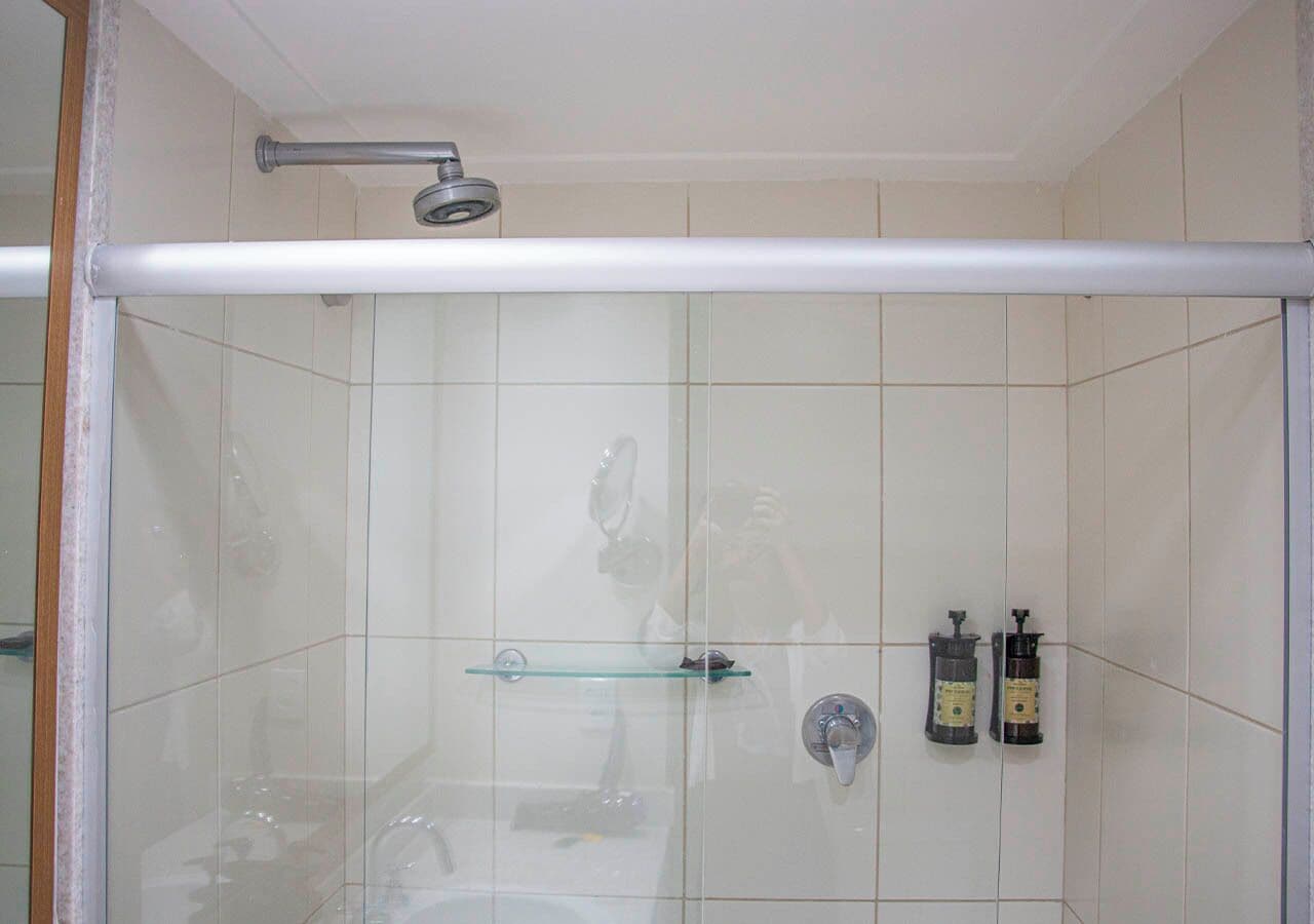 A shower with a glass door, a glass shelf, and two bottles of liquid soap.