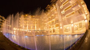 Un hotel de varios pisos con piscina y fuentes ornamentales.