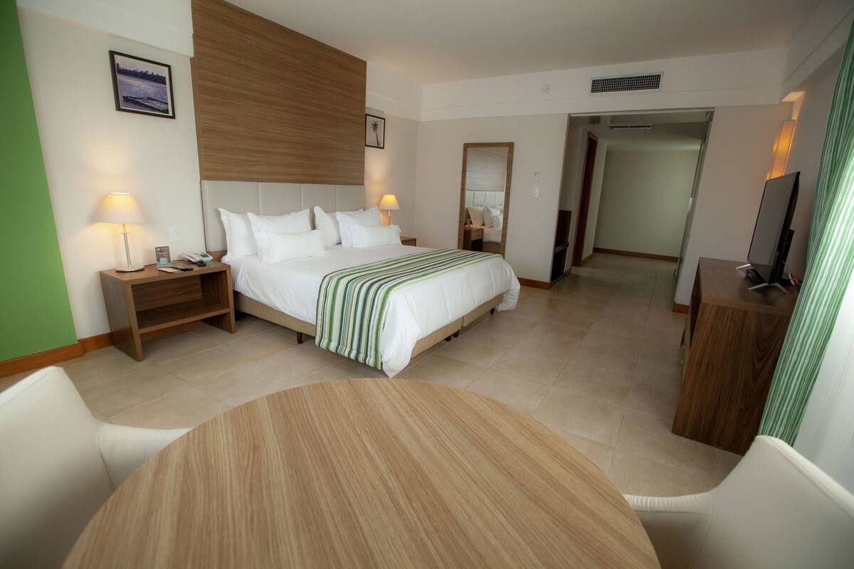 A hotel room with a bed, bedside tables, a round table, and a TV.