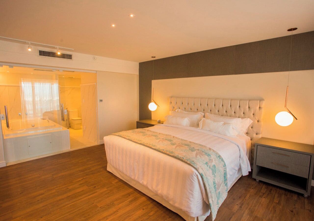 A modern bedroom with a large bed, bedside tables, and a bathroom with a bathtub and toilet.
