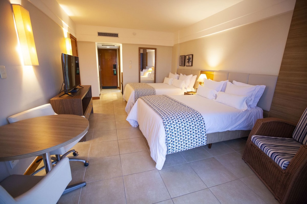 Ein Hotelzimmer mit zwei Betten, einem Schreibtisch, einem Stuhl, einem Fernseher und einer Lampe.