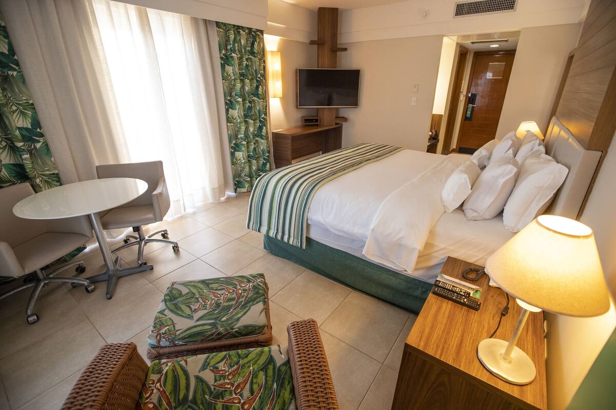 A hotel room with a bed, a desk, a chair, a TV, and a lamp.