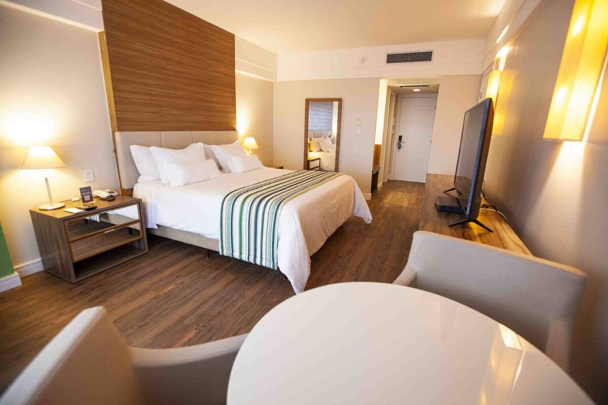 A hotel room with a bed, bedside table, lamp, TV, and a round table.