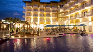 Un hotel con varios balcones, una zona de piscina con sillones de descanso y sombrillas.