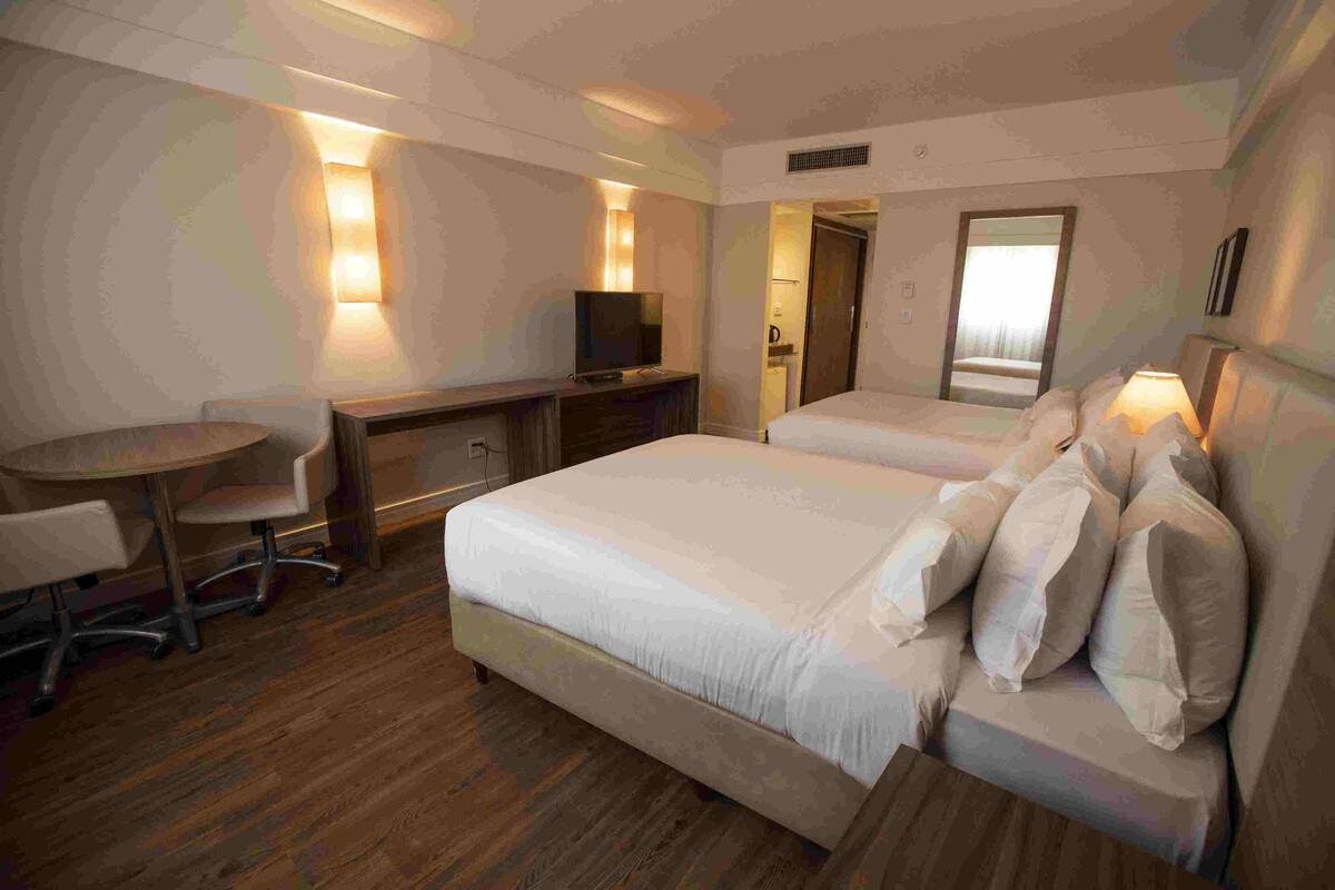 A hotel room with a double bed, a desk with a chair, a television, and a mirror.
