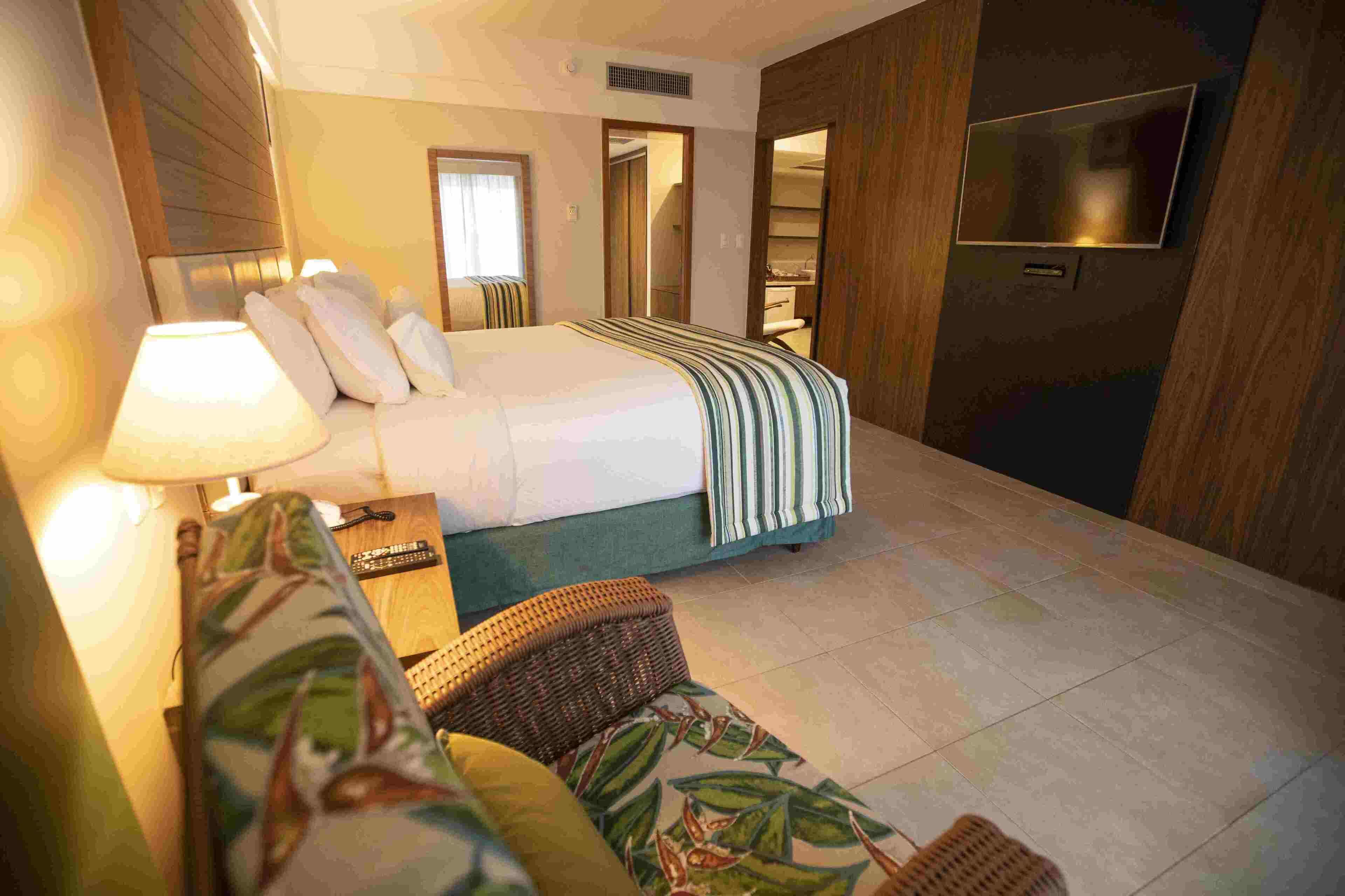 A hotel room with a bed, a TV, a sofa, and a bathroom visible through an open door.