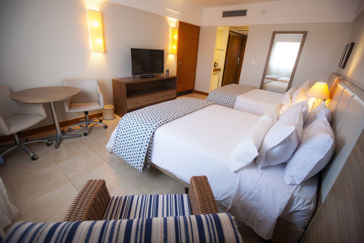 A hotel room with two beds, a TV, a desk, and a chair.