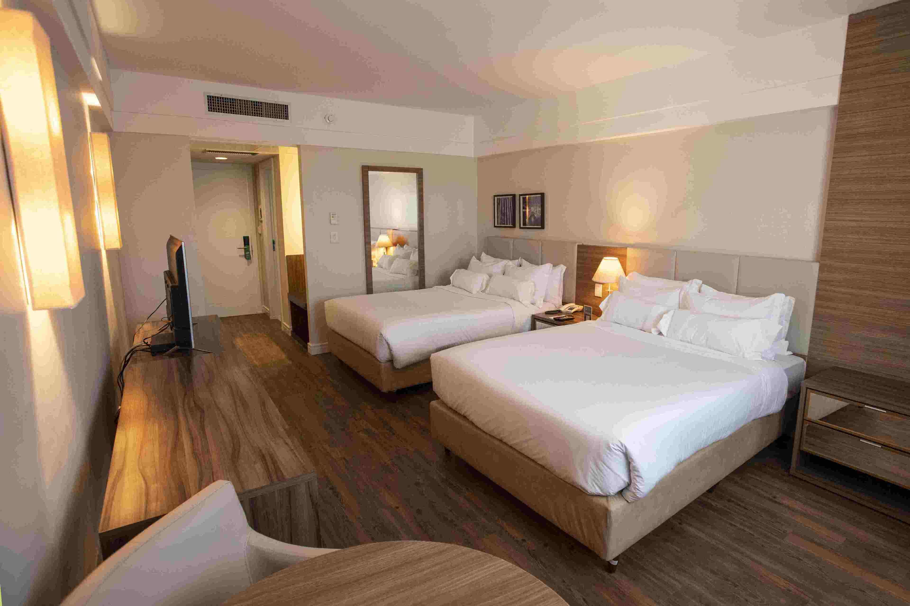 A hotel room with two beds, a desk, a chair, a TV, and a mirror.