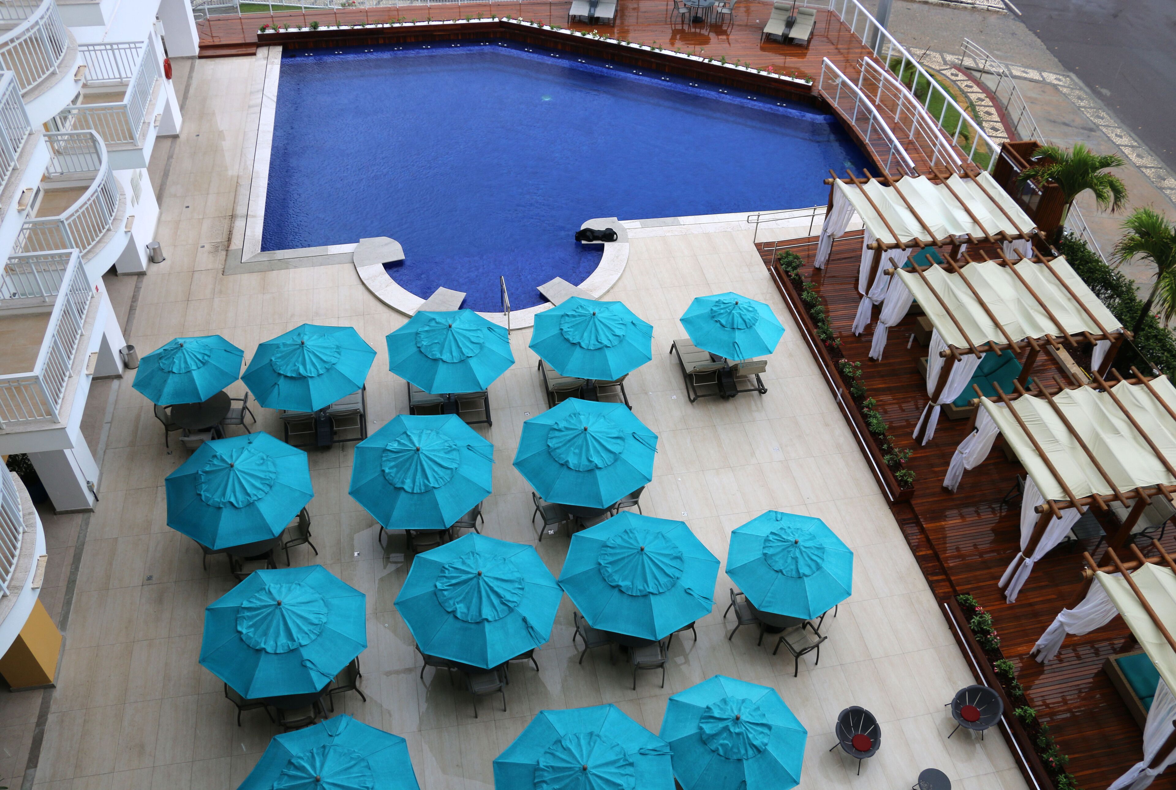 A rooftop pool area with multiple blue umbrellas and lounge chairs.