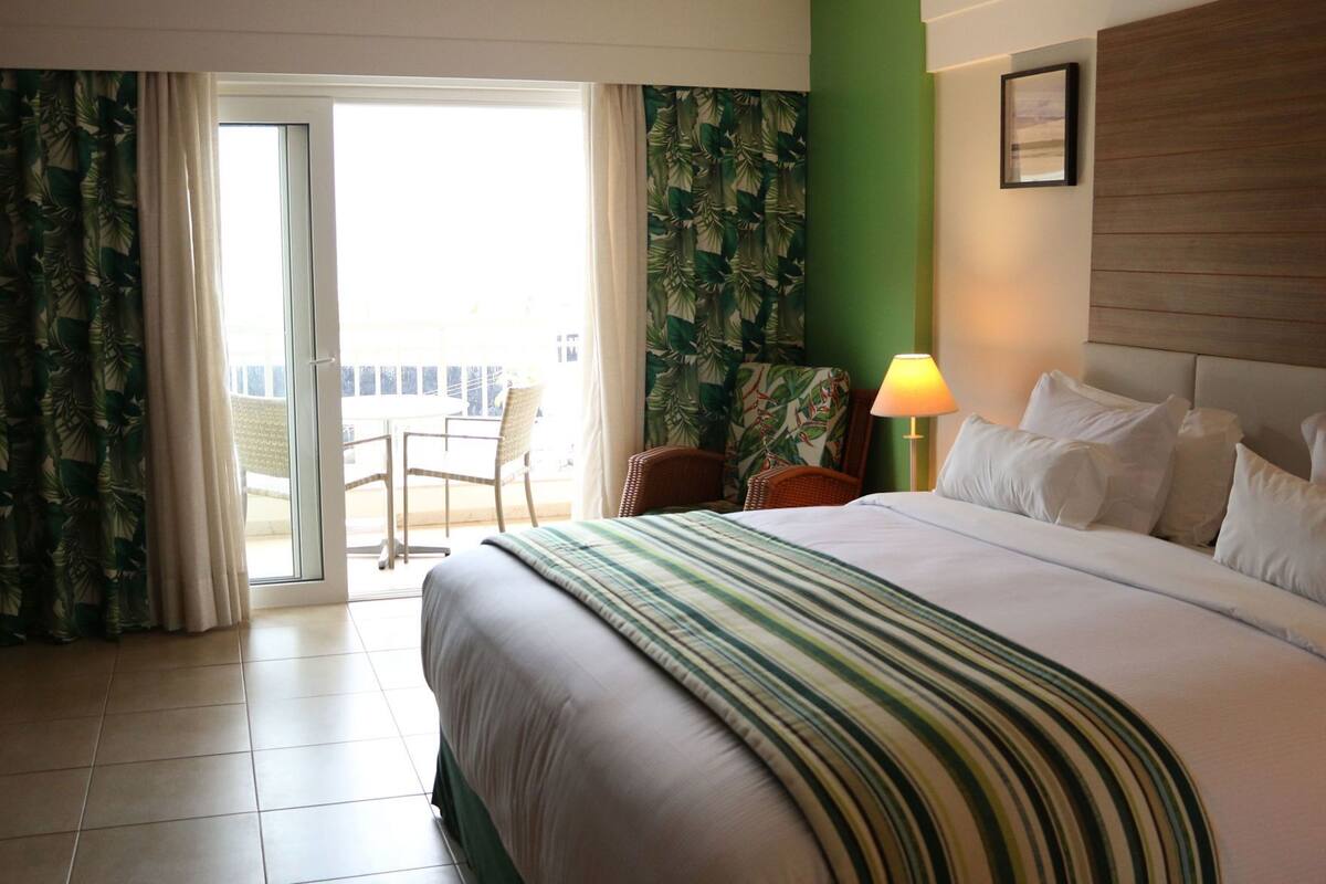 A hotel room with a bed, a chair, a table, and a view of the outside.