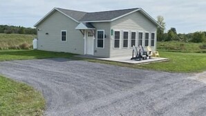 A single-story building with a sloped roof, a front porch with seating, and a gravel driveway. - #21 Isle View - Fishing, Sunsets, Beaches, Golfing (Alburgh)