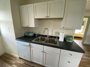 A kitchen with white cabinets, a black countertop, a stainless steel sink, and a dish rack.
