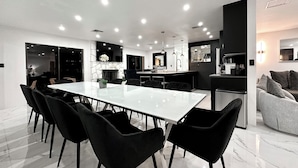 Une cuisine moderne dotée d’un îlot central, un coin repas avec une grande table et des chaises, et un espace de vie comprenant un canapé et une table basse.