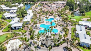 Vue aérienne d’un complexe hôtelier doté de plusieurs piscines, de palmiers et de bâtiments.