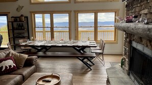 A dining area with a long table set for six, large windows with mountain views, a stone fireplace, and a cozy seating area with a leather couch. - Great Family Vacay! Luxury 6 BR 300 ft to Cupp Run Hot Tub In&Outdoor Fireplace (Snowshoe)
