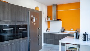 Una cocina moderna con gabinetes grises, una encimera blanca y una pared de acento naranja.