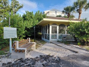 Un club de playa con un área de descanso cubierta, un cartel que detalla las normas para usar el ferry, y un edificio al fondo.