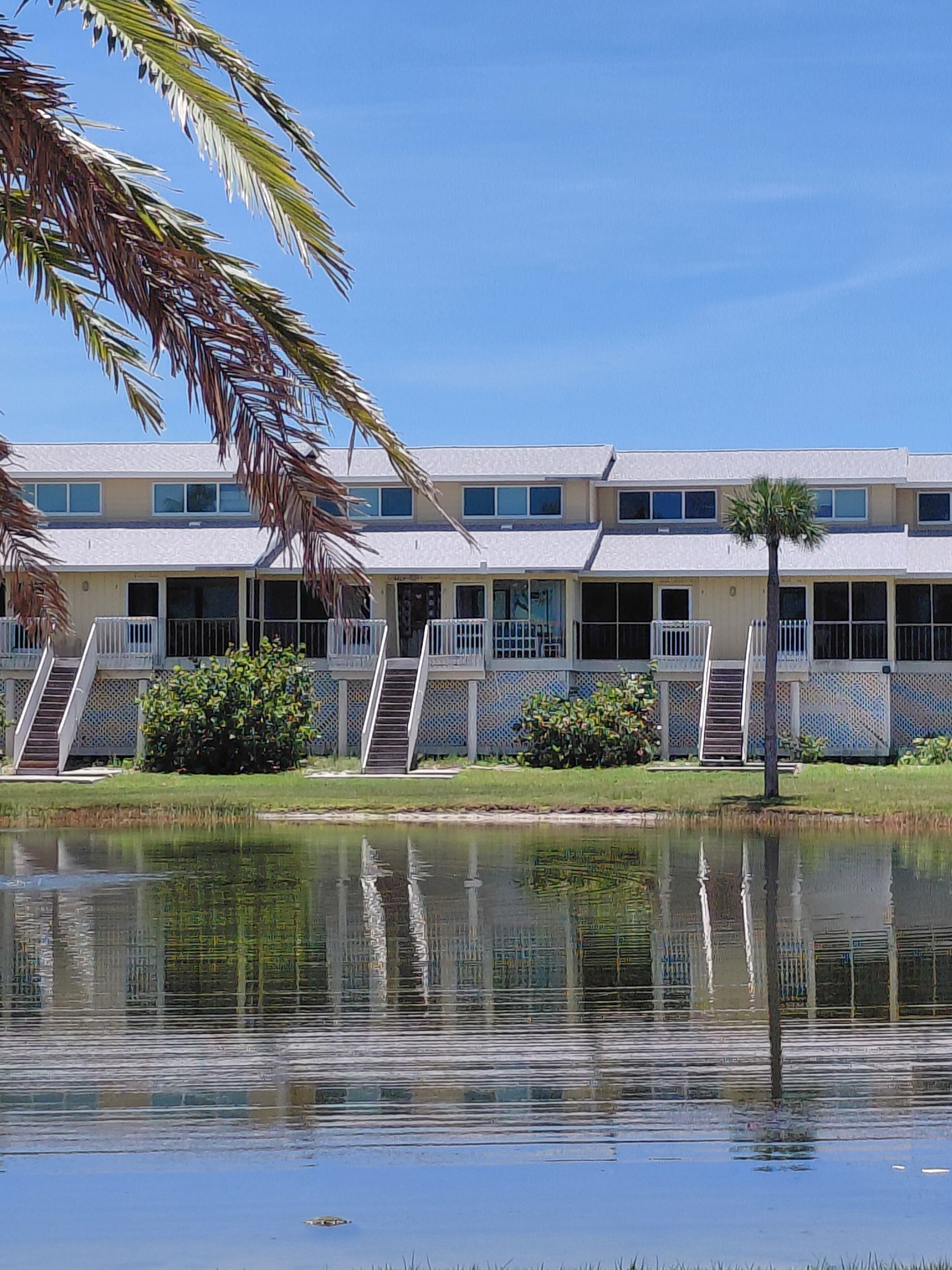 A multi-story hotel with balconies, a pool, and palm trees.