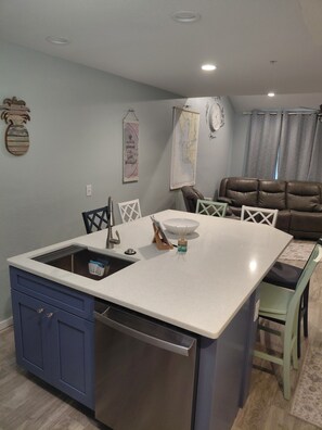A kitchen with a central island, a built-in dishwasher, and a dining area with chairs and a table.