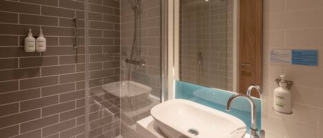 Une salle de bain moderne avec une douche à parois de verre, un lavabo blanc et deux bouteilles de gel douche de la marque Soak.