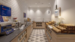 Zona de desayuno tipo buffet con diversas opciones de comida, incluyendo una estación de servicio para hacer panqueques y una selección de productos horneados.