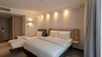 A modern hotel room with a large bed, bedside tables, a wall-mounted light, and a door.