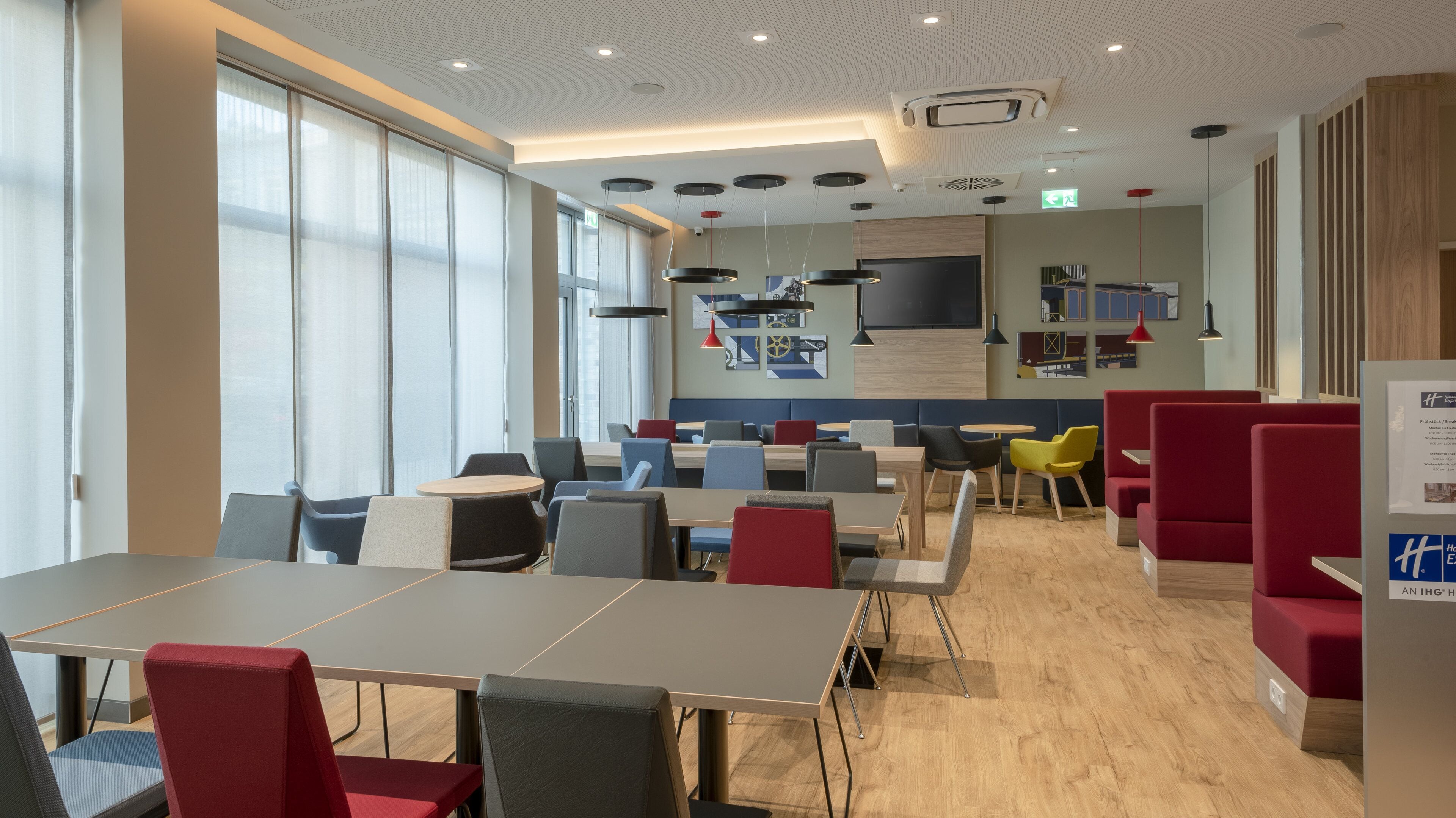 A modern dining area with tables and chairs, a wooden floor, and a large window with curtains.