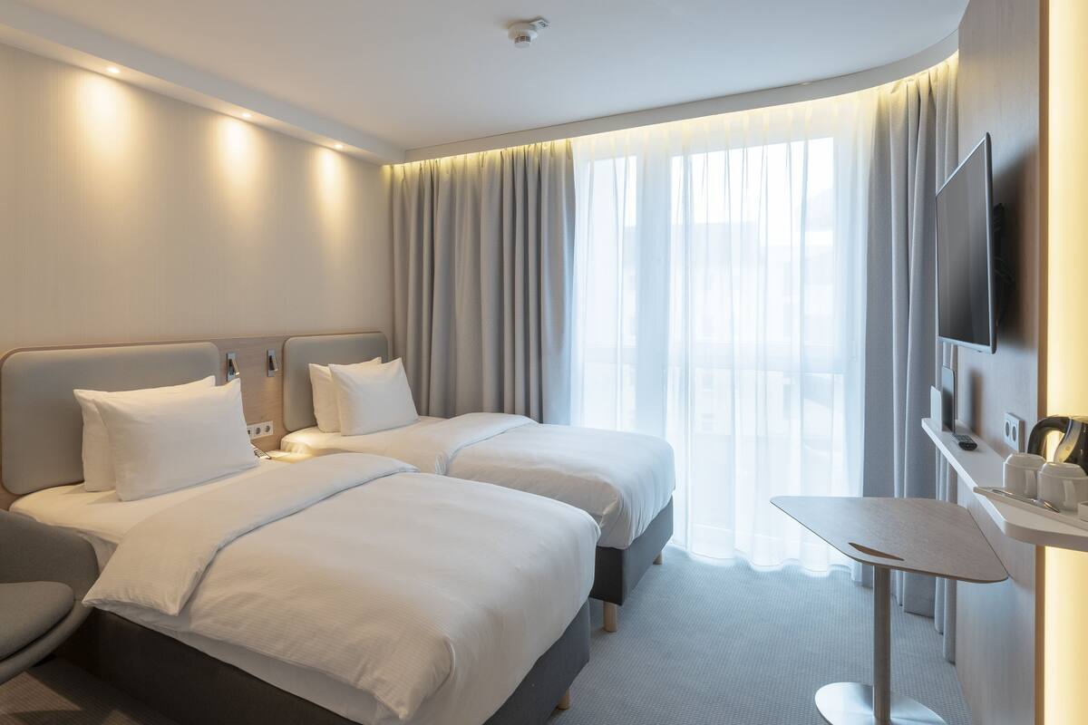 A modern hotel room with two beds, a seating area, and a TV.