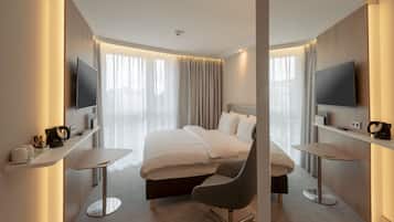A modern hotel room with a large bed, two bedside tables, a flat-screen TV, a coffee maker, and a chair.