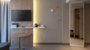 A modern hotel room with a flat-screen TV, a small table, a coffee machine, and a mirror.