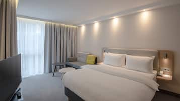 A modern hotel room with a large bed, bedside tables, a TV, and a window with curtains.