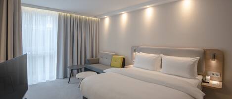 A modern hotel room with a large bed, bedside tables, a TV, and a window with curtains.
