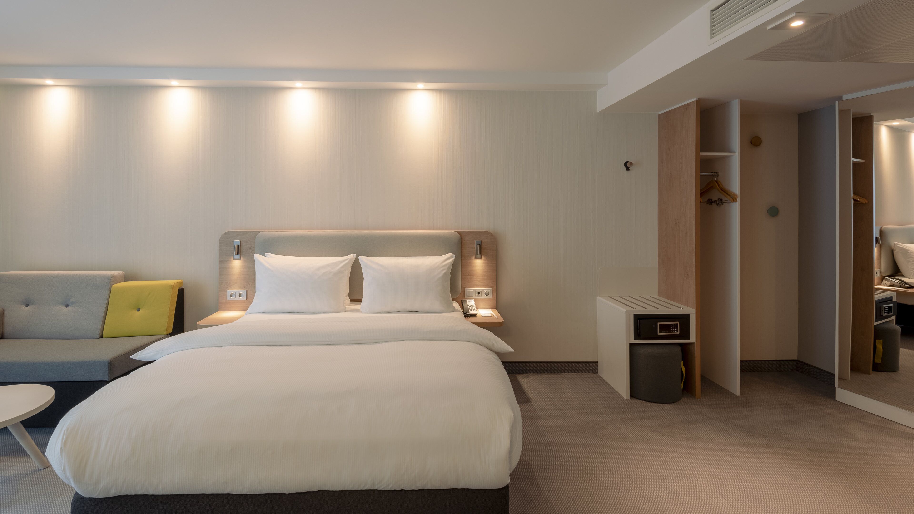 A modern hotel room with a large bed, bedside tables, a sofa, and a walk-in closet.