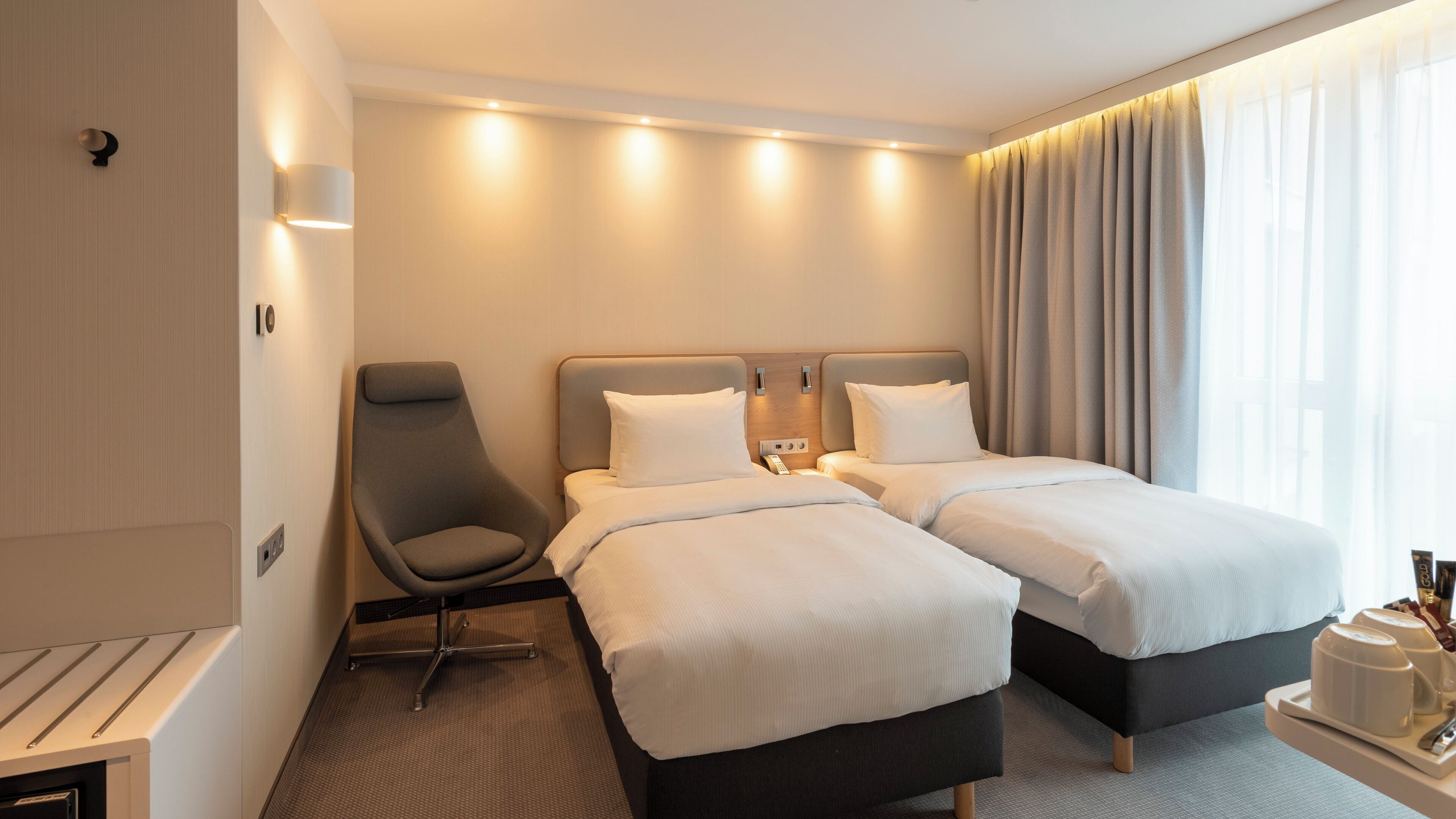 Een hotelkamer met twee bedden, een stoel, een bureau en een raam met gordijnen.