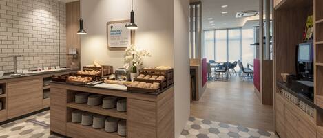 A modern kitchen area with a buffet setup, including bread, pastries, and a coffee station.