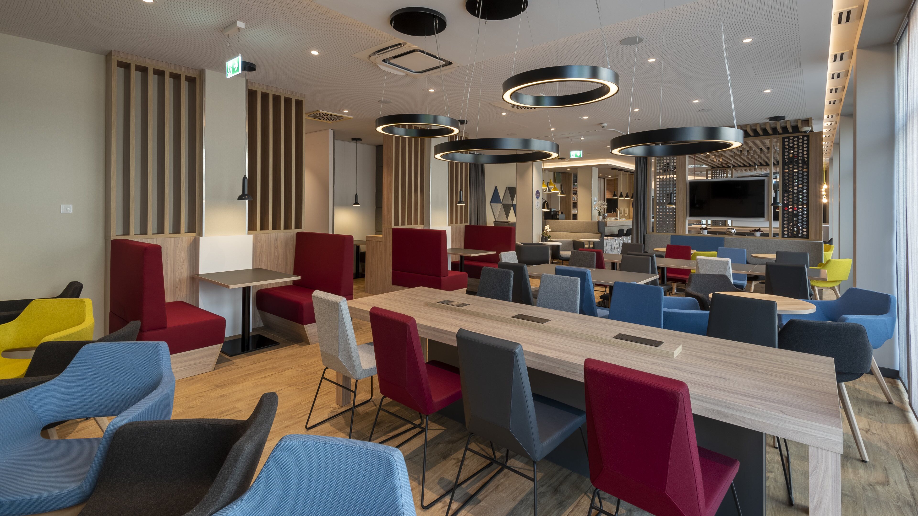 A modern dining area with a long wooden table, red and blue chairs, and a variety of seating options.
