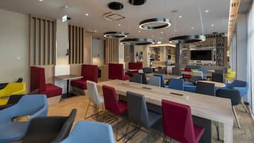 Un comedor moderno con una mesa de madera larga, sillas rojas y azules, y diferentes opciones de asientos.