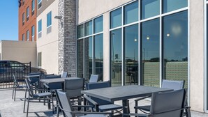 An outdoor patio area with tables and chairs, a stone pillar, and large windows. - Holiday Inn Express & Suites Watertown by IHG (Watertown)