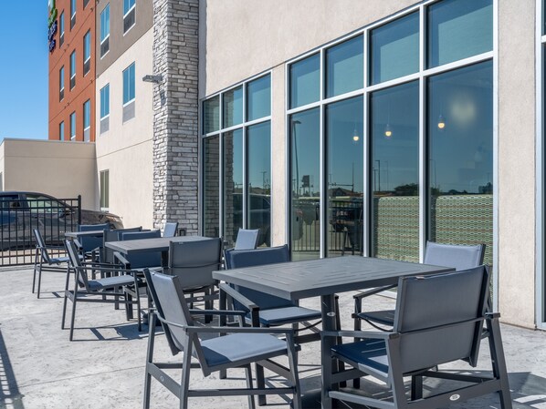 An outdoor patio area with tables and chairs, a stone pillar, and large windows. - Holiday Inn Express & Suites Watertown by IHG (Watertown)