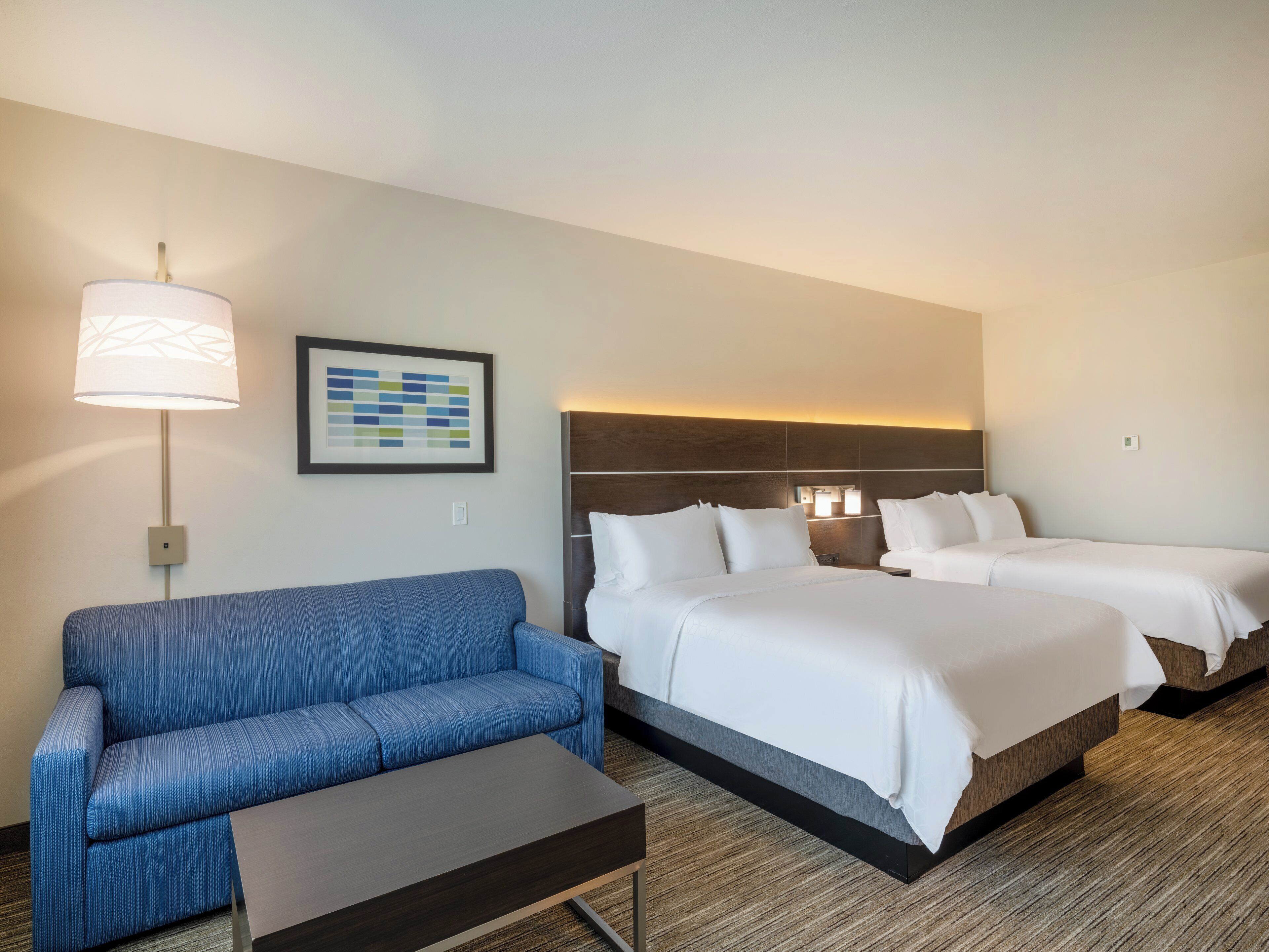 Een hotelkamer met een blauwe bank, twee bedden, een nachtkastje en een lamp.