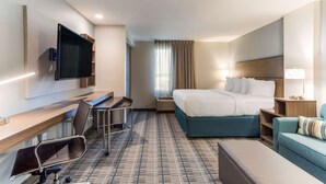 Una habitación de hotel con cama, escritorio, silla, televisión y ventana con cortinas.