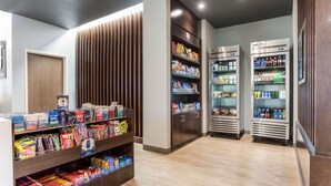 Quiosco de aperitivos y bebidas con estantes llenos de diversos snacks y refrescos, y dos dispensadores refrigerados para bebidas.